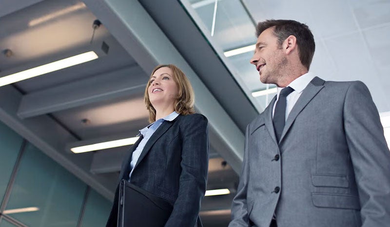 A man and a woman in business suits walking together, discussing something.