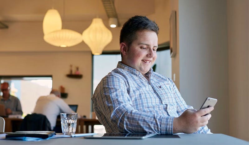 A man smiling while using his phone in a bright office space.
