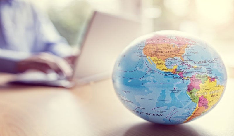 A close-up of a globe with a person working on a laptop in the background.