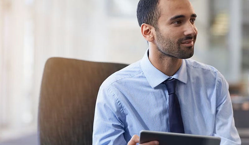 A professional reviewing data on a tablet while seated at a desk.