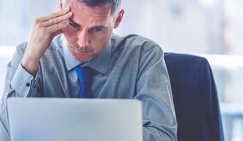 A man sitting at his desk with a stressed expression while working on a laptop.