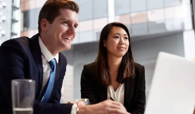 Two professionals smiling and discussing over a laptop in a modern office.
