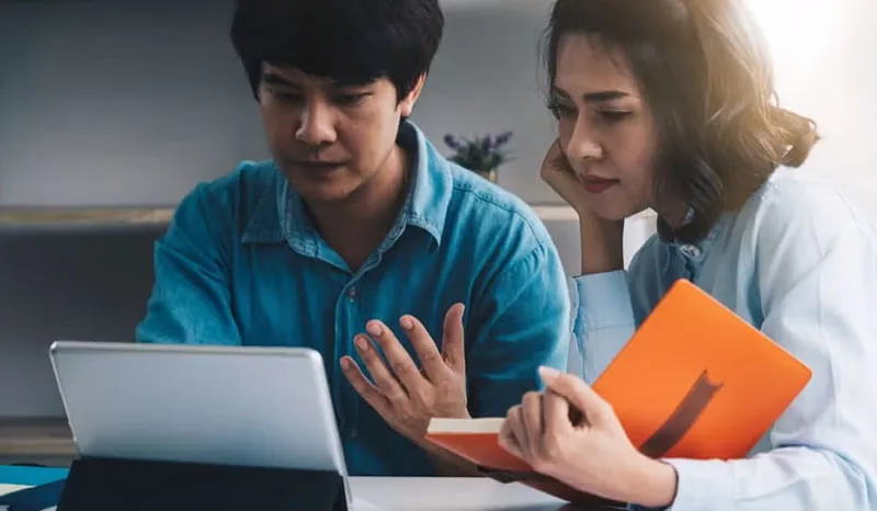 Two people working together on a laptop, one of them gesturing.