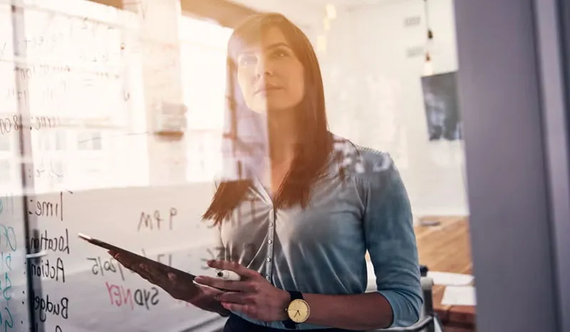 A woman writing and planning ideas on a glass whiteboard in an office.